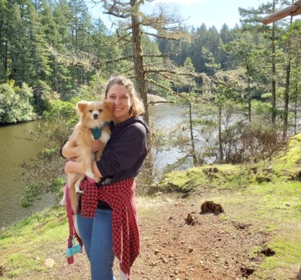 Lindsay holding Minnow next to a river. Behind them some evergreen trees.