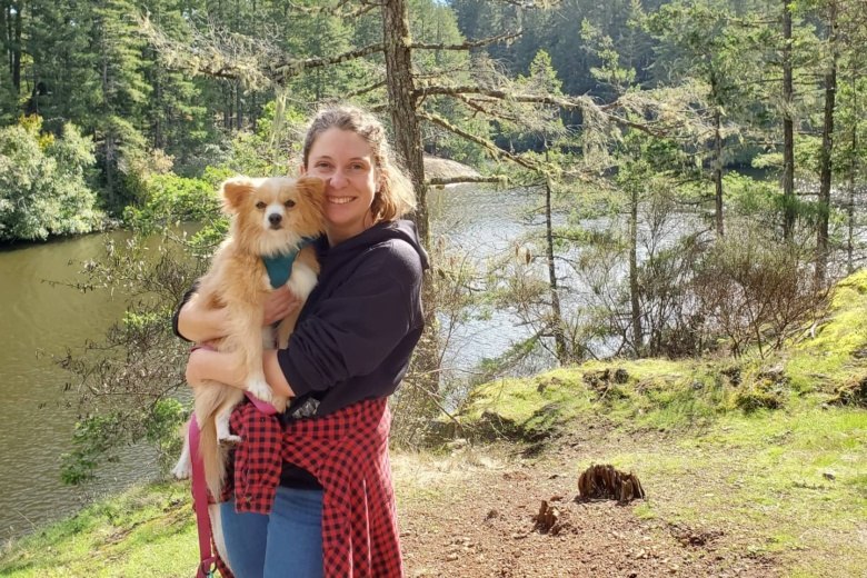 Lindsay holding Minnow next to a river. Behind them some evergreen trees.